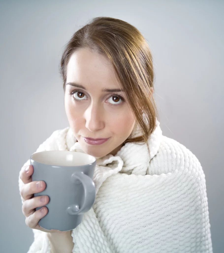 Eine Frau, die in eine weiße Decke eingehüllt ist und eine Tasse in der Hand hält